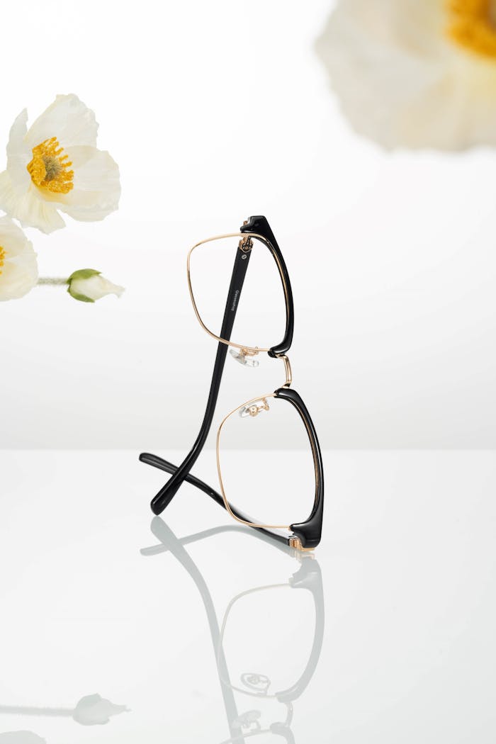 Stylish black and gold eyeglasses with white flowers on a reflective surface.