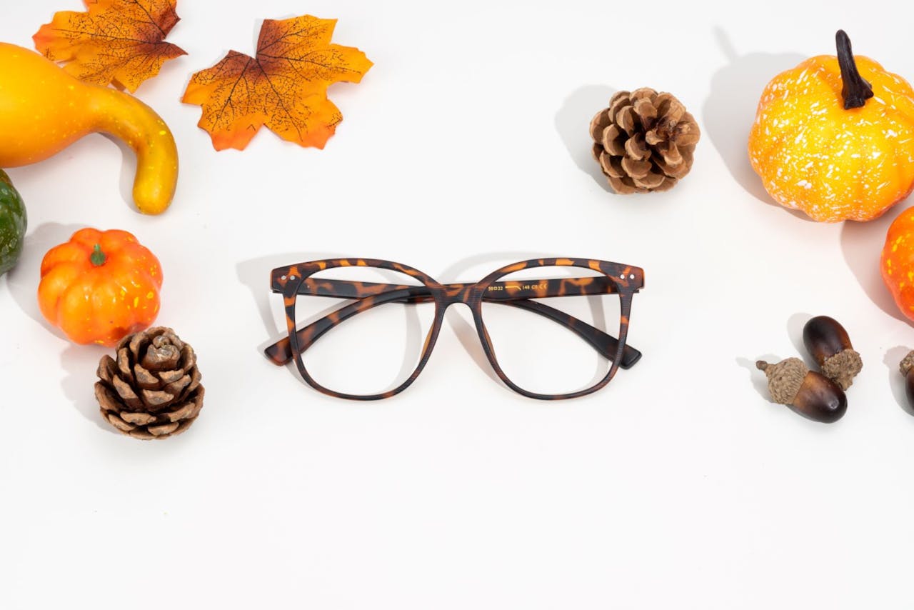 Tortoiseshell glasses surrounded by fall decorations like gourds and pinecones on a white background.